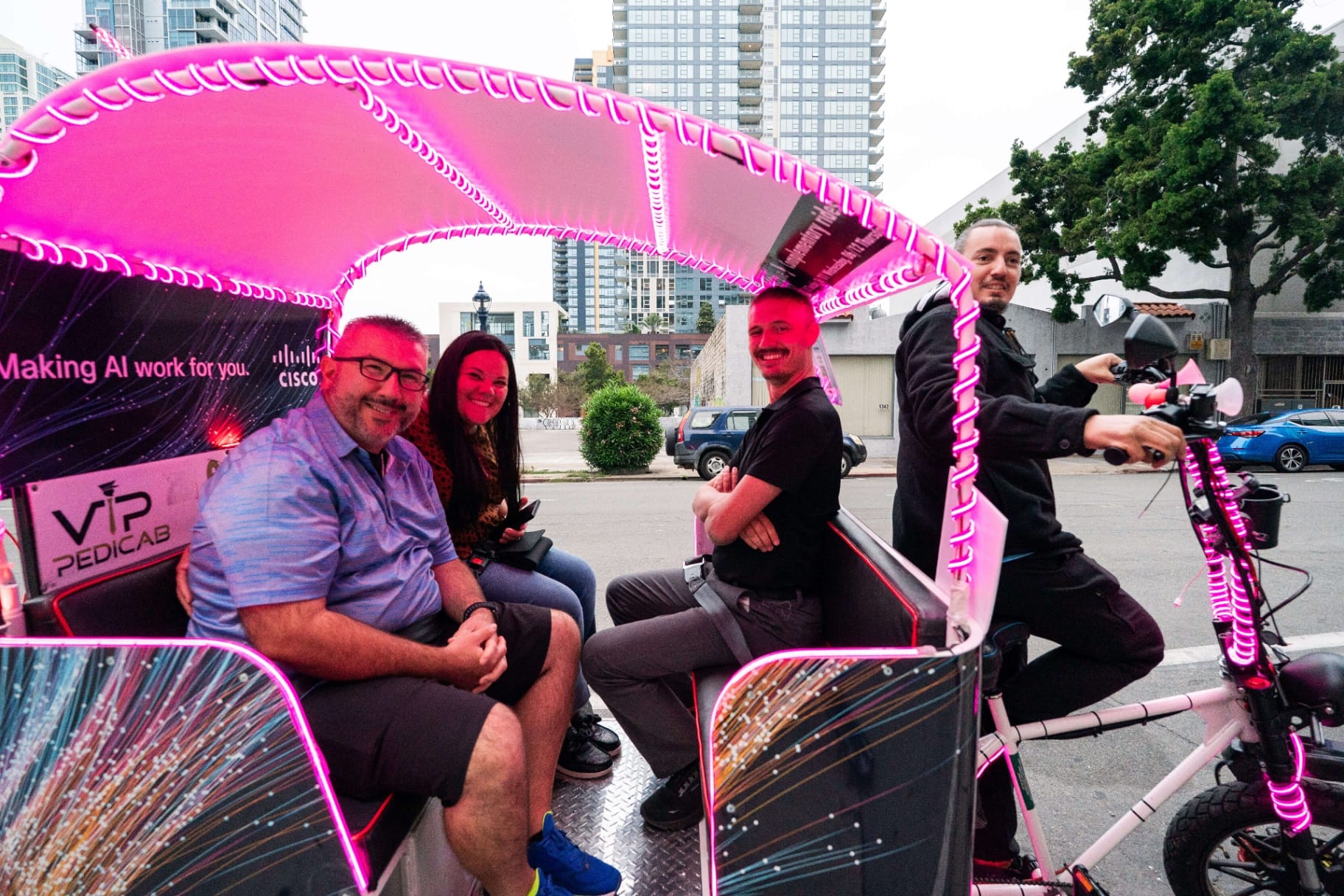 Happy passengers in Cisco Live pedicab with pink LED lights San Diego