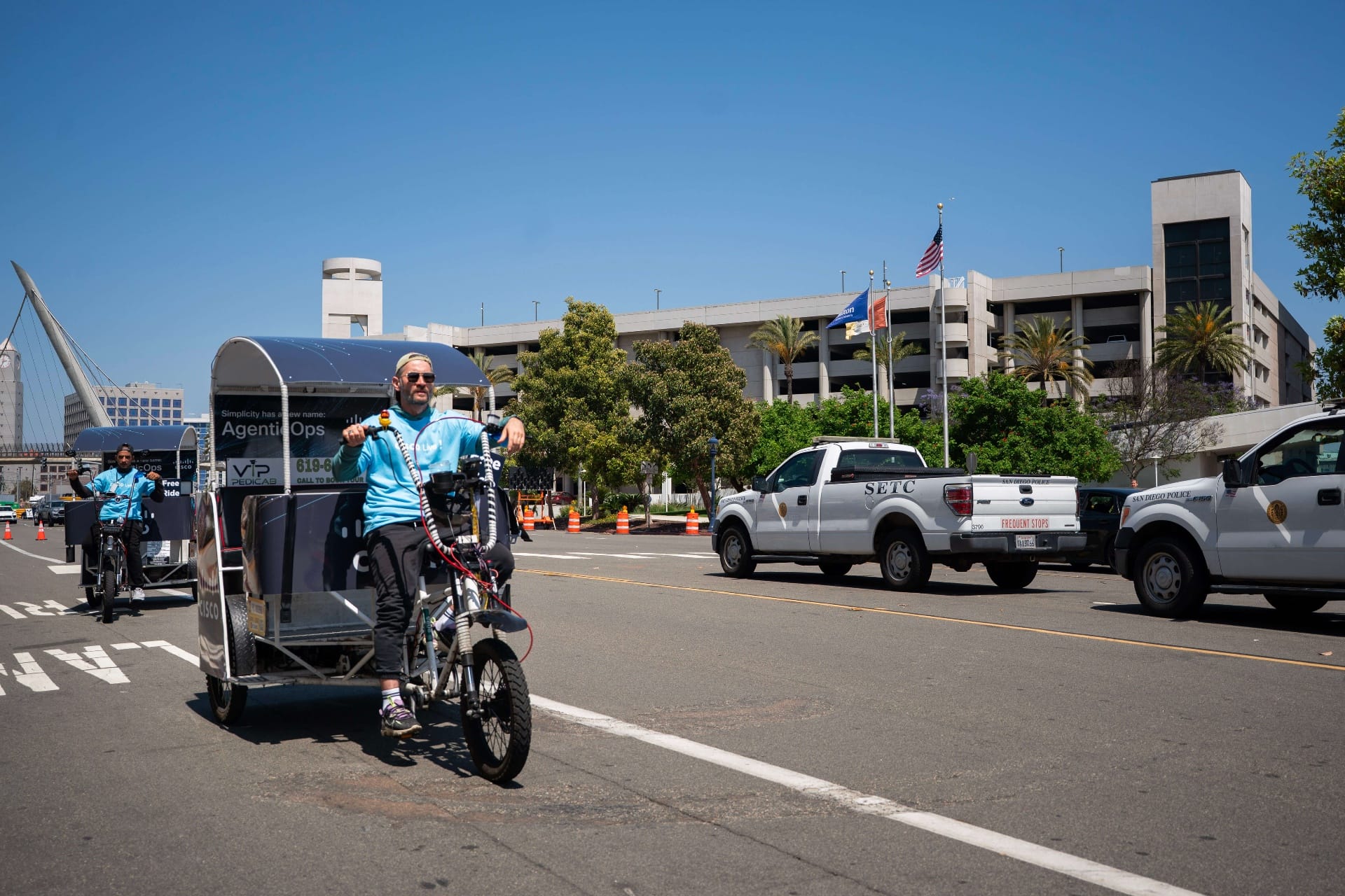 Cisco AgenticOps branded pedicab riding past San Diego police vehicle