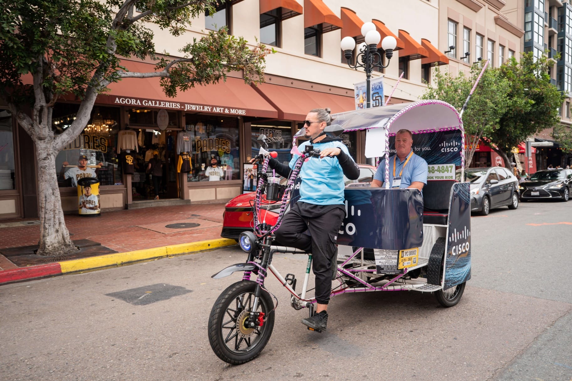 Cisco pedicab driver riding passenger past Padres shops Gaslamp Quarter