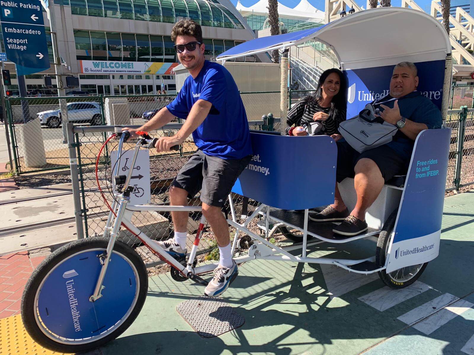 UnitedHealthcare pedicab driver smiling with passengers at an Embarcadero conference in San Diego