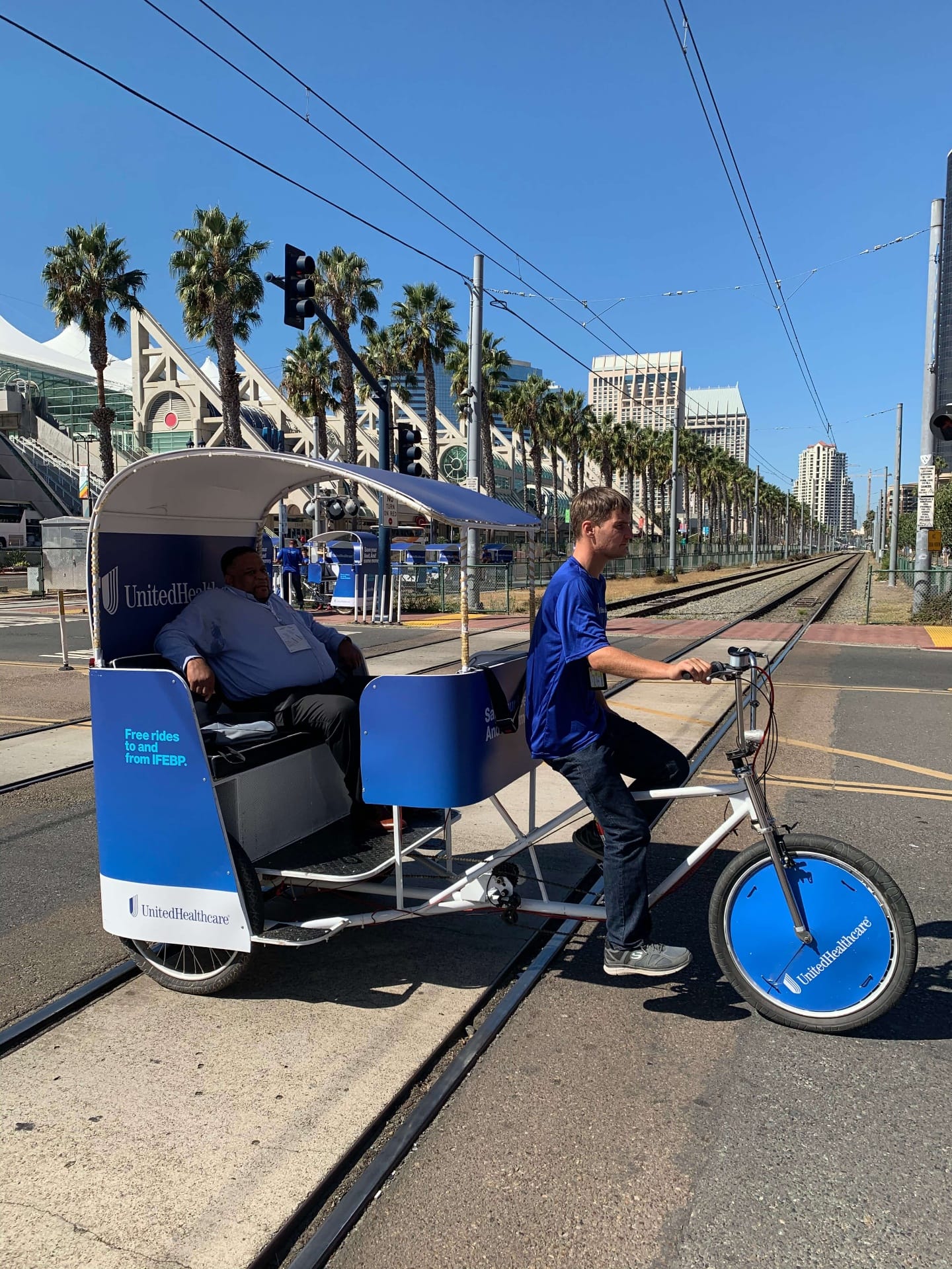 UnitedHealthcare pedicab rider with passenger near Convention Center trolley