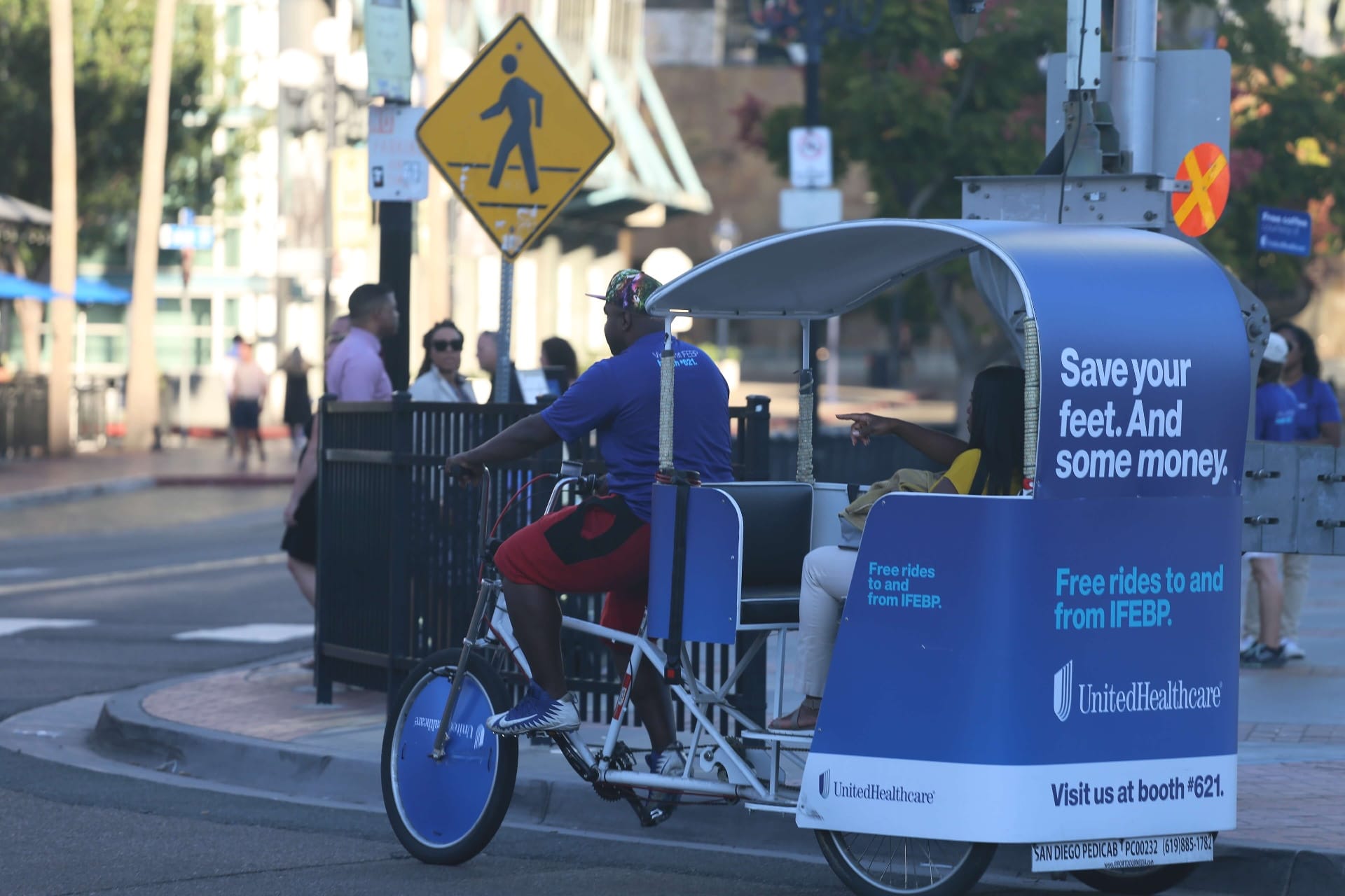 UnitedHealthcare pedicab rider with passenger at downtown San Diego crosswalk